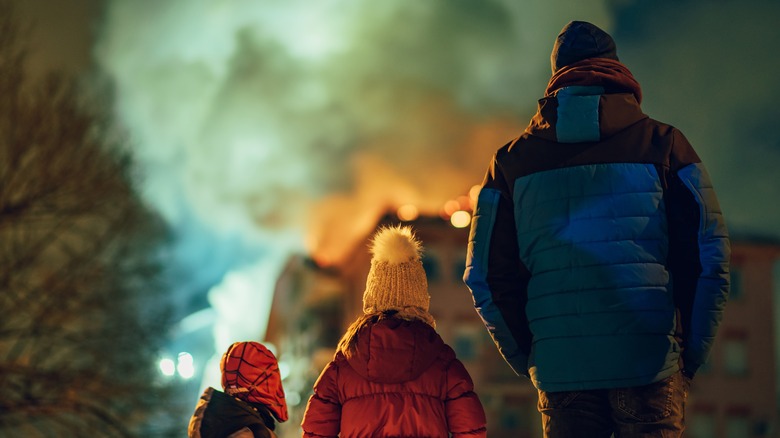A man and two children standing side by side looking at a burning building