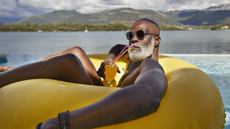 A senior man sipping a drink while reclining in a floatee in a lake