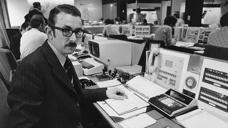 man working at a banking desk in the 1970s