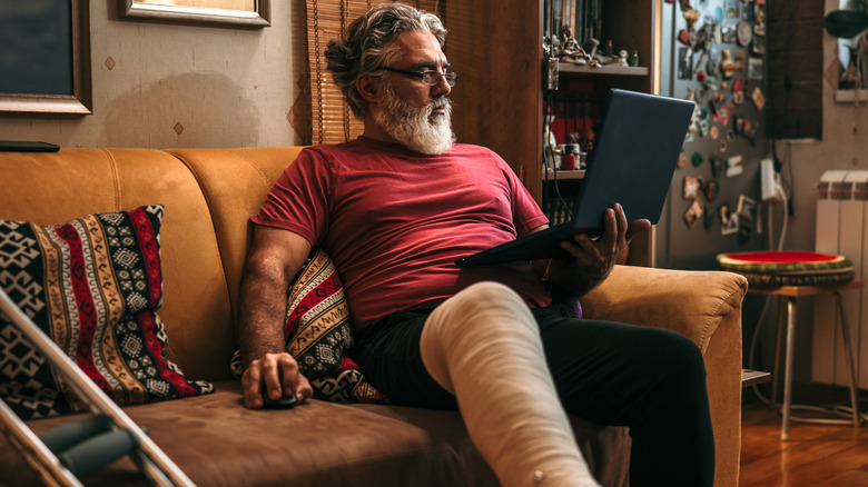 Man with a broken leg looking over medical bills on his laptop