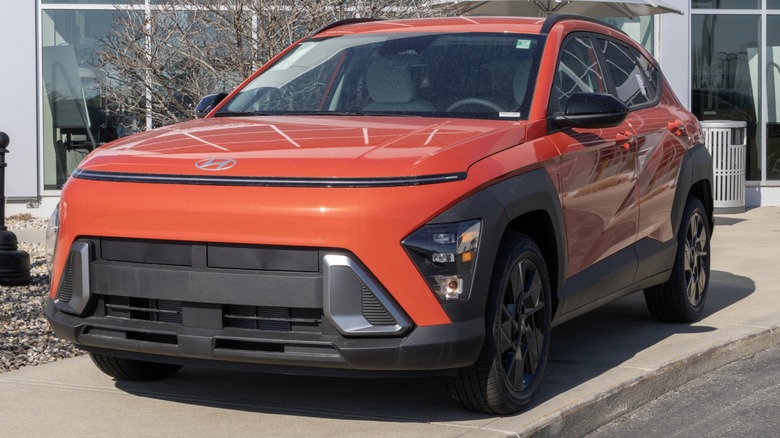 Orange Hyundai Kona parked outside a dealership, shown from the front three-quarter angle