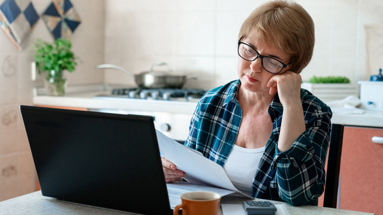 A depressed mature woman sitting in front of a laptop and calculator.