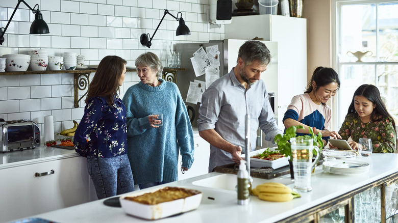 Five people gathered around a kitchen island in a white kitchen.