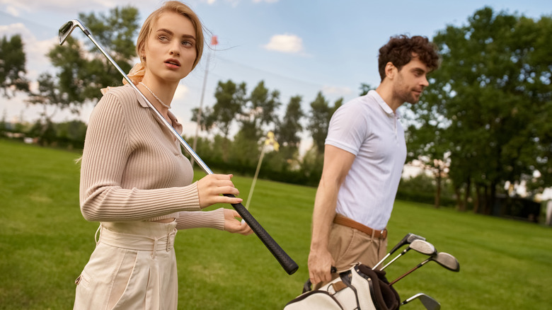 A man and woman in elegant attire walk on a lush green golf course.