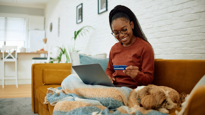 A young woman shopping online at home with her dog in her lap