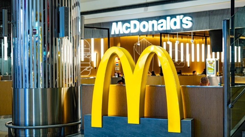 A newer McDonald's is located inside of an airport terminal with the giant golden arches outside and tables seen in the background..