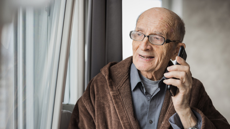 Senior man having a phone conversation and looking through the window while doing so