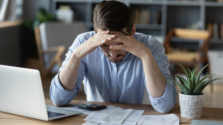 Frustrated young man holding head over a stack of documents and calculator