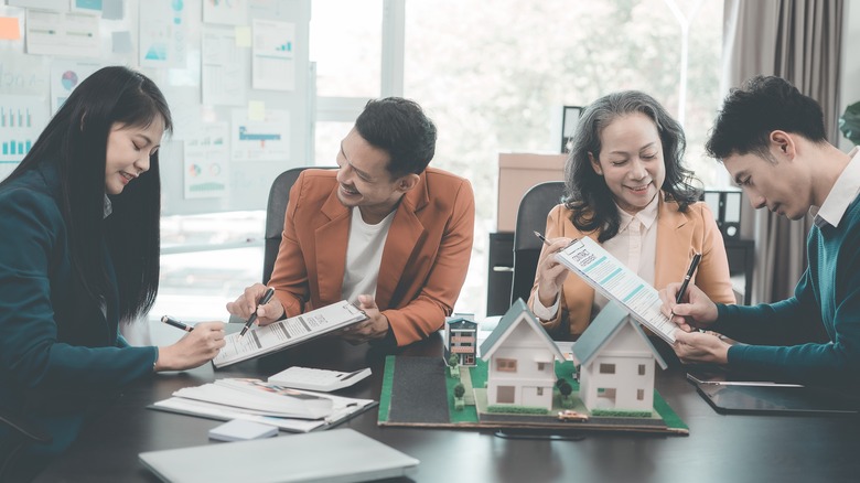 Real estate professional meeting with wooden house models with documents and laptops discussing the construction of family homes for a housing project.