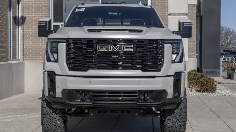Front view of a white GMC pickup truck with a large black grille parked outside a dealership