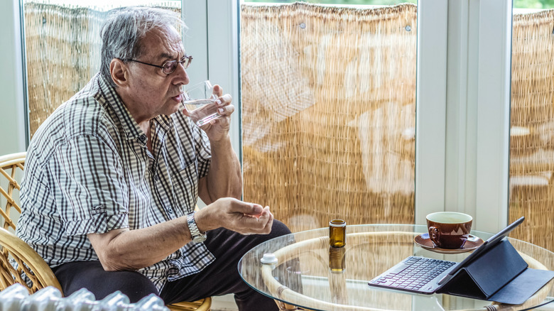 A senior man taking pills in front of an open tablet