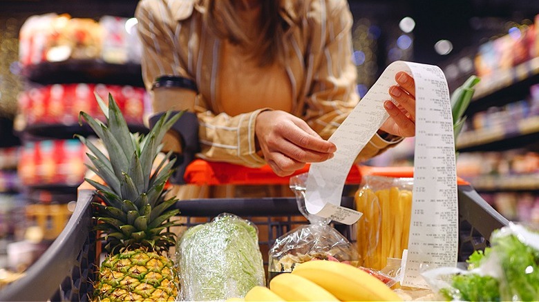 Person reading receipt over grocery cart