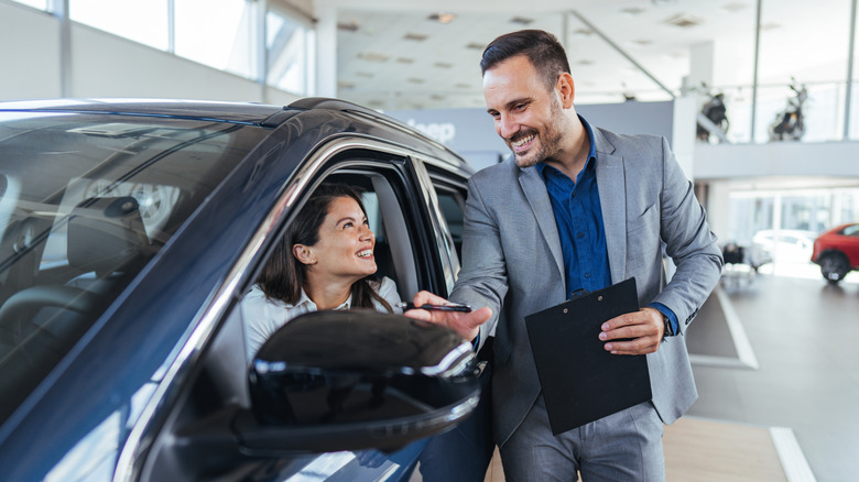 A luxury car salesman discusses a vehicle with a woman behind the wheel