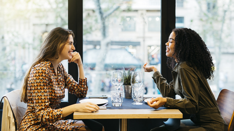 Two young smiling women sitting on a restaurant table