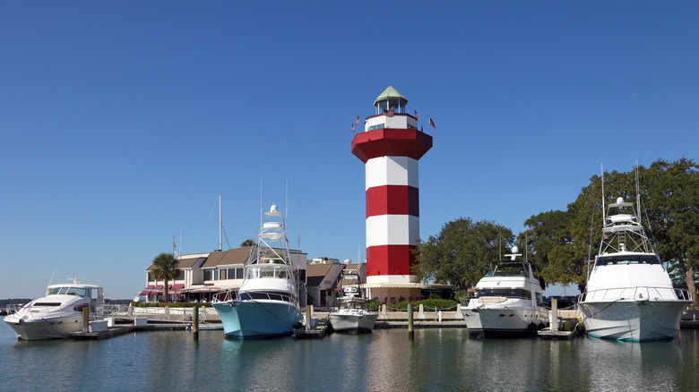 Harbour Town boats in the harbor, near Hilton Head's famous red-and-white-striped lighthouse, against a blue sky.