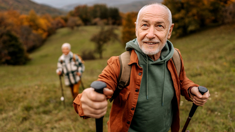 A smiling senior man hiking uphill with a senior woman behind him.
