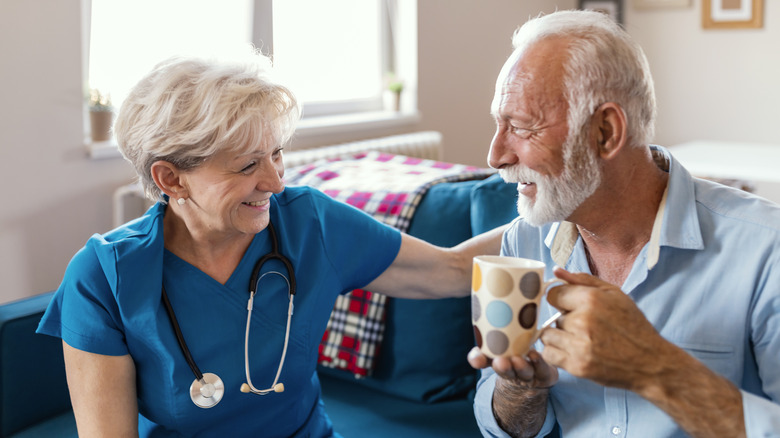 Happy senior man talking with friendly nurse at geriatric ward.