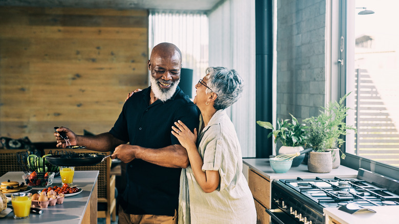 A smiling mature couple in a brightly lit kitchen preparing a meal