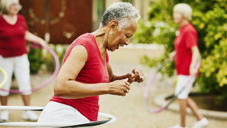 A senior woman laughing while hula hooping with two elderly women with hula hoops in the background