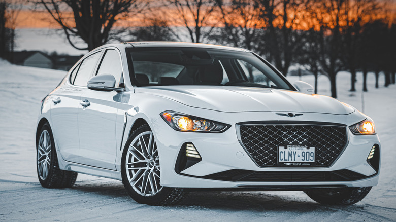 A white Genesis G70 parked outside in the snow at sunset.