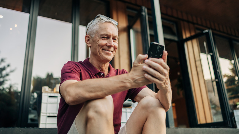 Mature man uses a phone while sitting on a cozy sidewalk cafe in summer