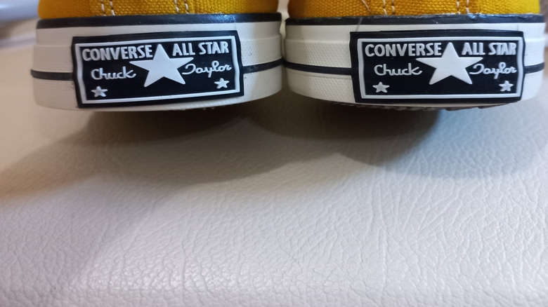 Person holding up the heels of fake yellow Converse.