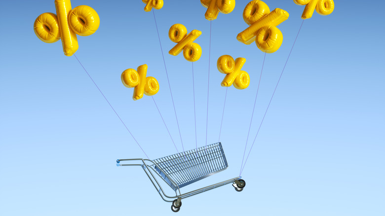Digital generated image of balloons in shape of percent sign holding and moving up with shopping cart against white background.