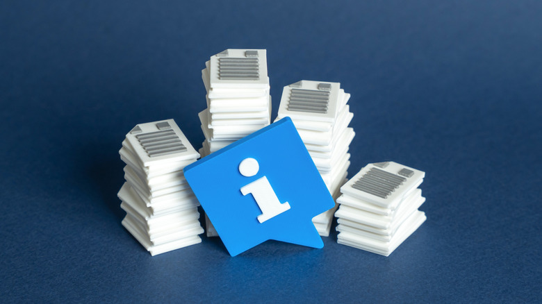 Toy blue information bubble resting on a stack of physical document images.