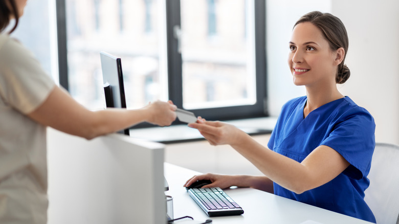 A person handing a receptionist a card at a medical office
