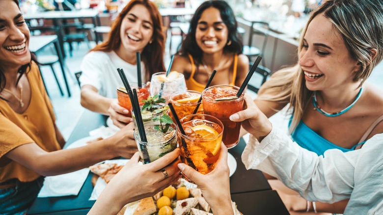 an ethnically mixed group of young women toast using cocktails