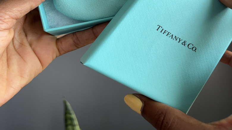 female hands with yellow nail polish holding open a Tiffany blue box