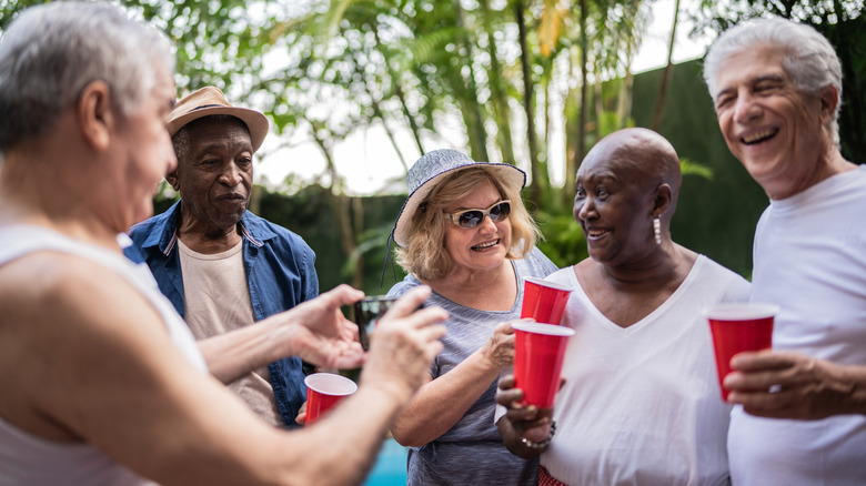A happy group of mature friends smiling while one takes a photo with their phone.
