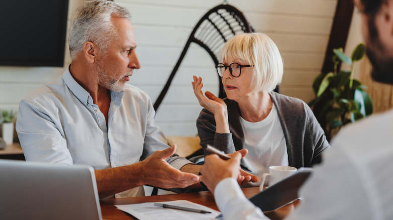 Unsure older couple look at each other across the table from man
