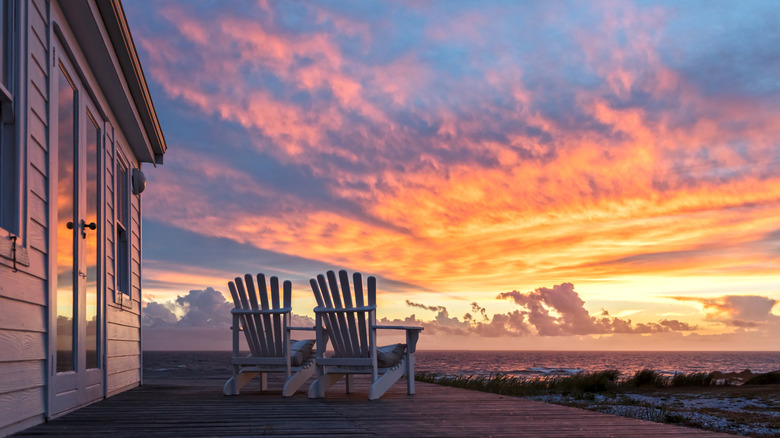Two Adirondack chairs on the wooden deck of an oceanfront cottage