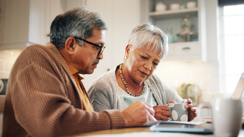 Senior couple looking at letter while drinking coffee.