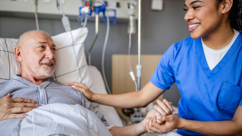 An old man lies on hospital bed while holding nurse's hand