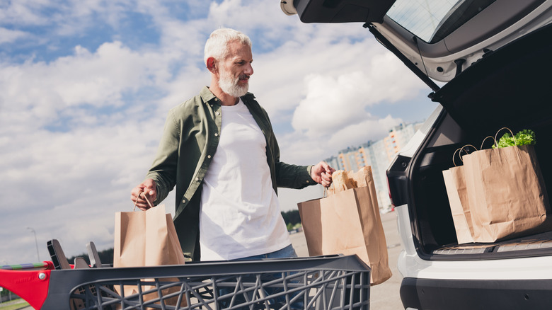 A mature man loading the trunk of his car with groceries.