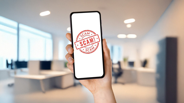 Hand holding smartphone displaying scam alert stamp on white screen.