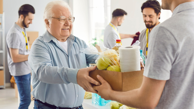Old man receives box of supplies with some younger men in the background.
