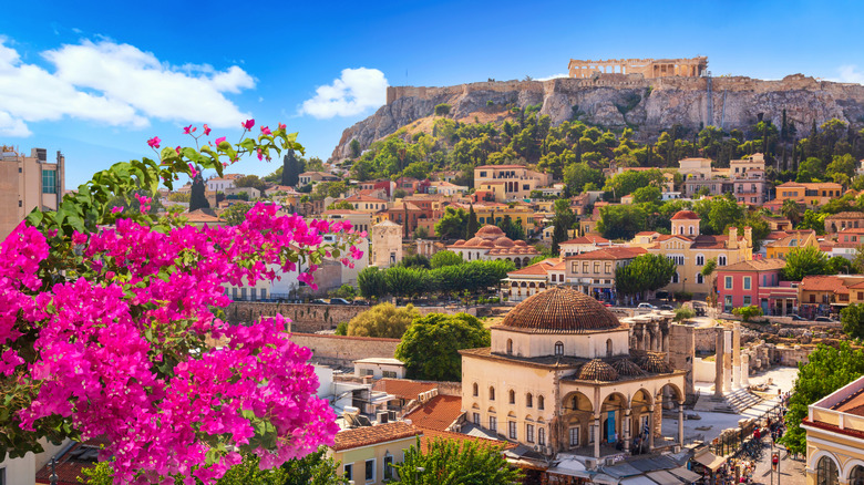 A view of Athens, Greece with pink bougainvillea flowers in the foreground and buildings stretching out in the distance