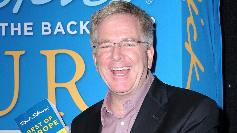 Rick Steves posing for a photo while holding a travel book