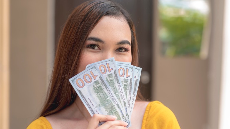 A lady covering her smile with five hundred dollar bills she is holding in her hands