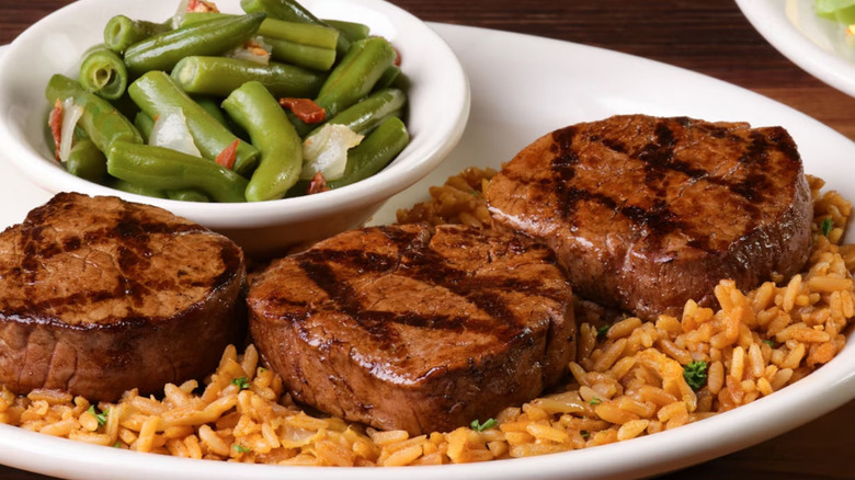 A plate of three Texas Roadhouse filet medallions over seasoned rice, nestled next to a side of green beans.