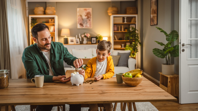 Father and son add money to piggy bank.