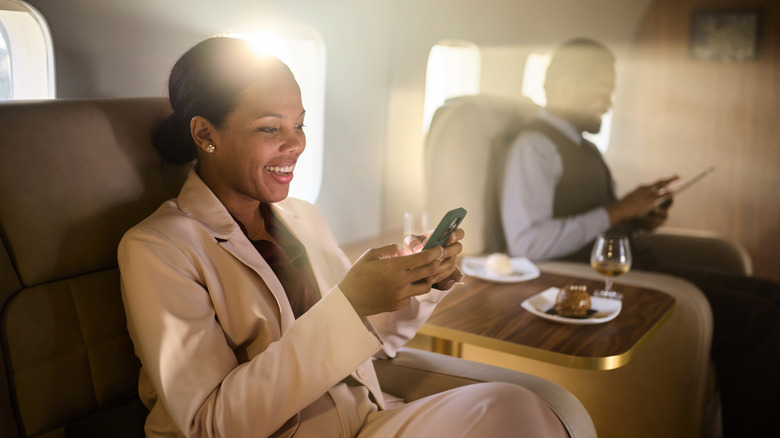 Happy businesswoman sending a text on smartphone during travel by corporate jet.