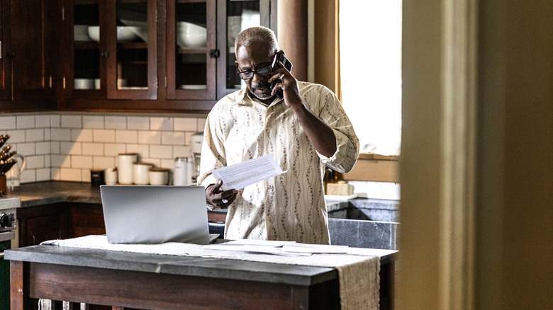 Man looks at paperwork while on phone in kitchen