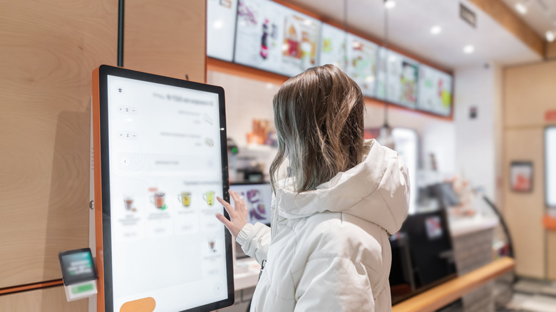 Woman using self-serve screen at fast food restaurant.