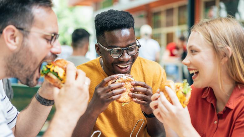 Friends eating burgers and fries and have fun in outdoor restaurant.