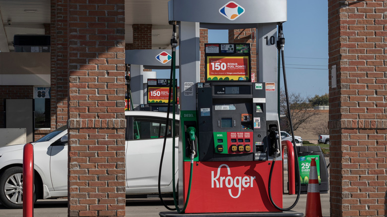 A white sedan parked between fuel pumps at a Kroger gas station
