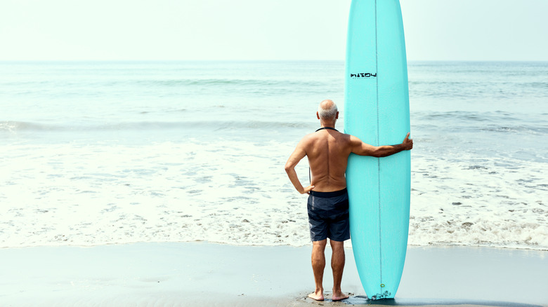 senior holding a surfboard at beach